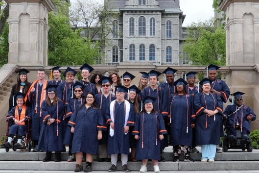 A group of students smile for a photo outdoors wearing navy blue graduation regalia.