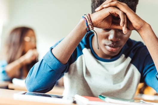 Depressed young African American student sitting in class with his head in his hands