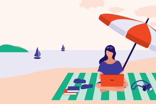 Woman sitting at beach working on computer with several books beside her