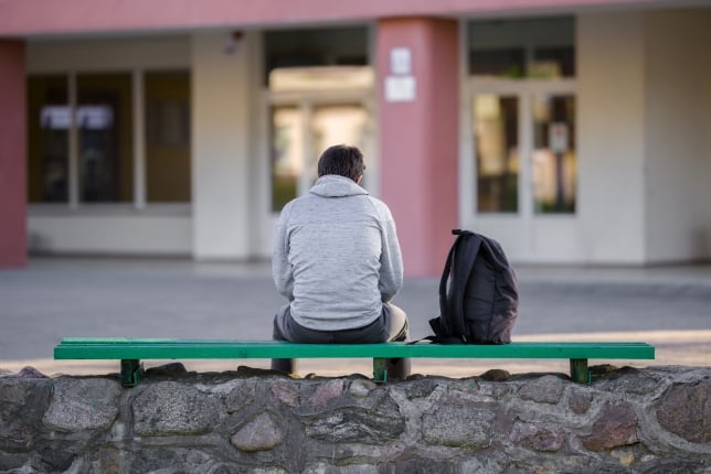 A student sits alone on a bench, facing away from the camera