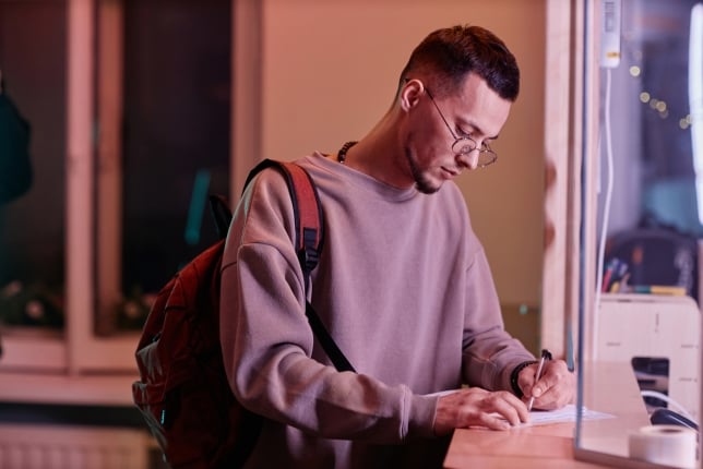 Young man filling out form at a desk at college. 