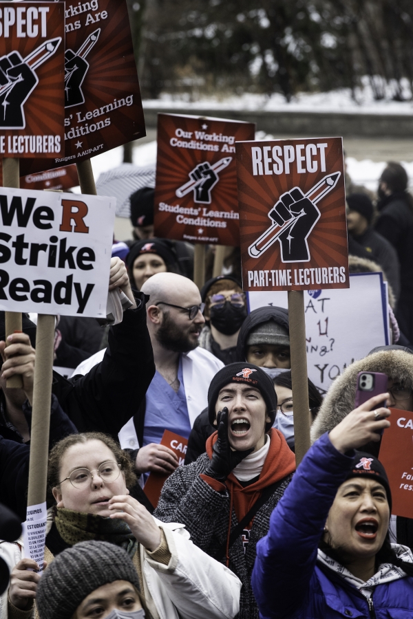 Striking staff members at Rutgers are dressed for cold weather and holding red and white signs, some of which say "We R strike ready" and "Respect."