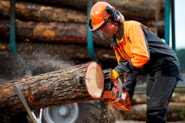 A female student wearing protective gear uses a chain saw to trim a log.