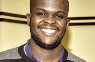 A smiling dark-skinned man with a beard and mustache looking at the camera.