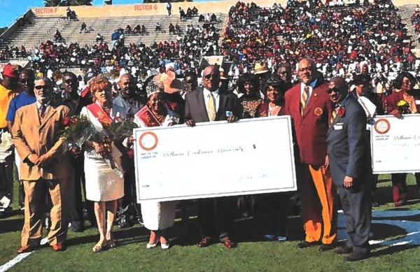 A group of Bethune-Cookman University alumni and university officials in suits pose with a large check.