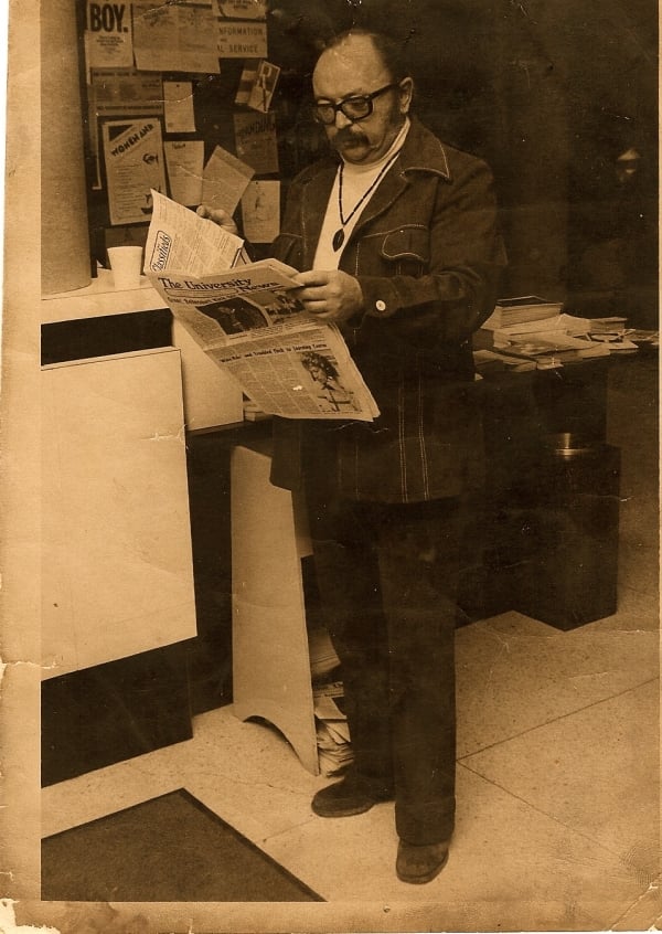Sepia photo of a man in glasses and a suit reading a newspaper