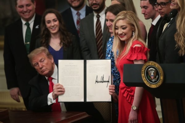 Trump, surrounded by seemingly college students, holds a two pieces of way