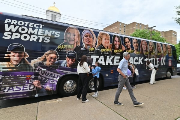 People walk by a bus that says protect women’s sports
