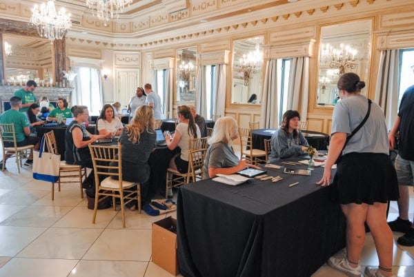 People sit at tables in a chandelier-lit ballroom