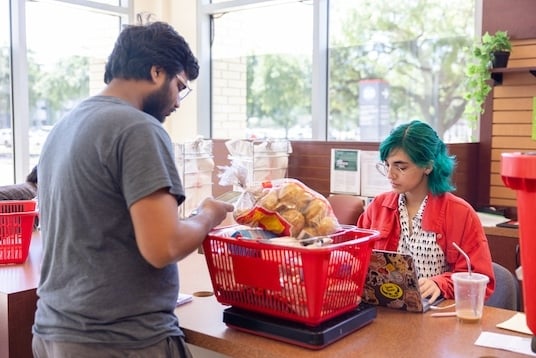 A student shopper weighs his shopping cart with the help of a student employee