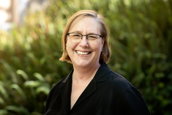 Lisa MacLeod smiles for a headshot wearing a black collared shirt. Lisa has short blonde hair and thin framed glasses.