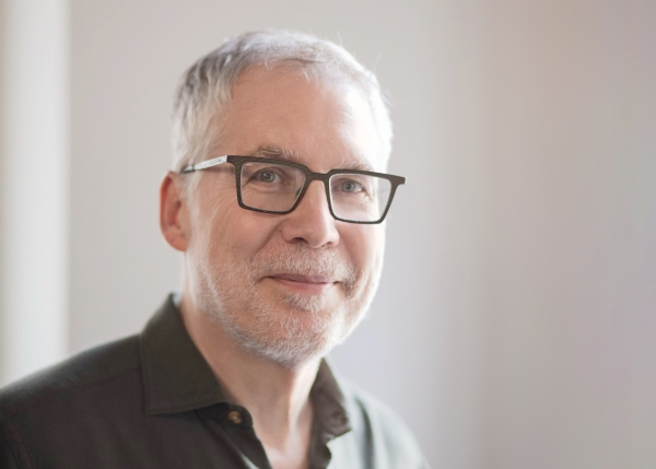 A light-skinned man with short gray hair and rectangular glasses.