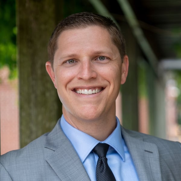 Kevin McClure, a light-skinned man wearing a suit and tie and smiling widely.