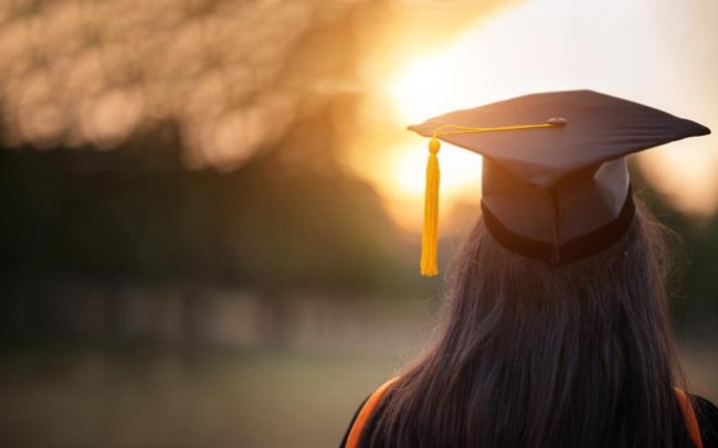 Premium Photo | A student wearing a graduation cap and gown smiles at the  camera.