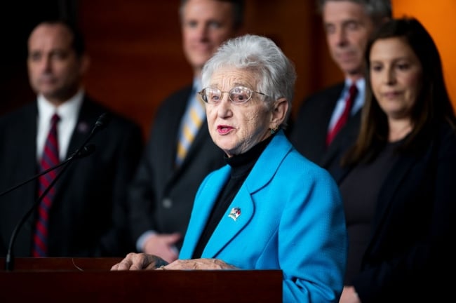 Virginia Foxx, a white woman with short white hair, stands at a podium in a blue blazer.