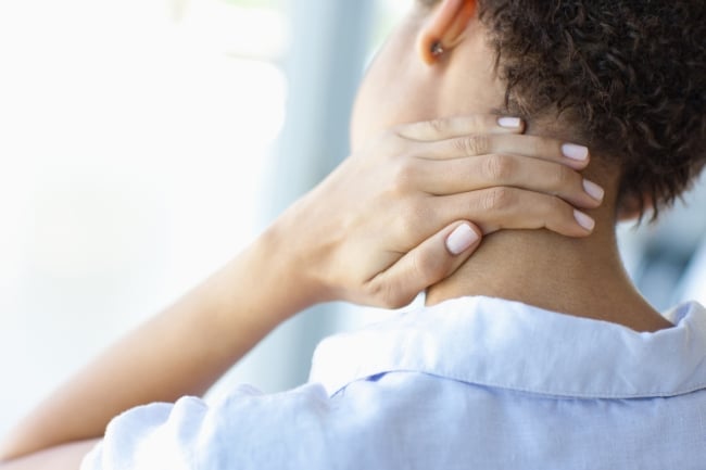 Close-up color photo of young woman rubbing her neck, shown from the back (face not shown)