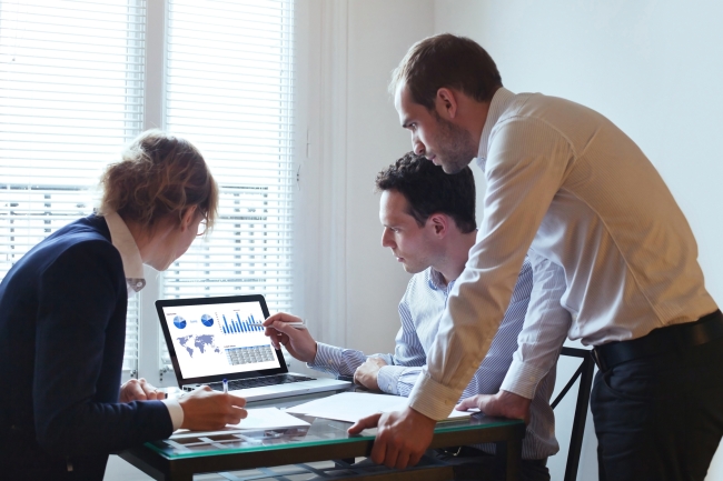 Three professionals gather around a laptop to look at data.