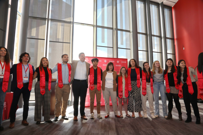 A group of students links arms wearing red graduation stoles.