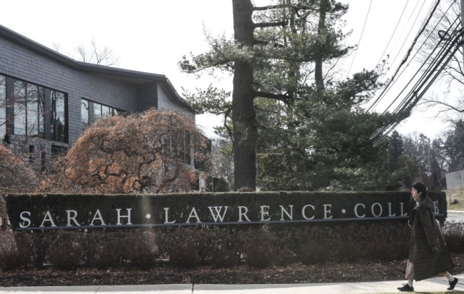 A sign for Sarah Lawrence College, as person in a jacket walks past.