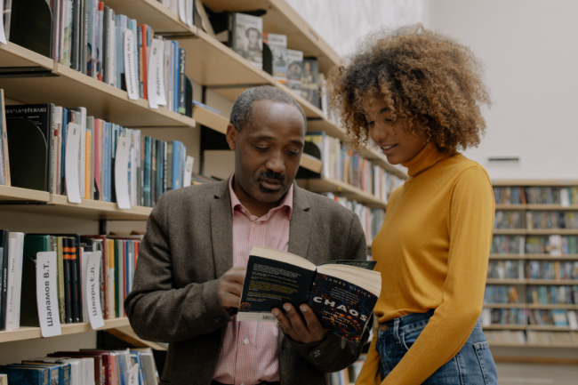 A female student looks at a book with a male professor.