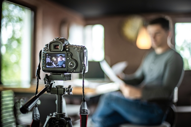 A man sits in front of a camera to deliver a speech.