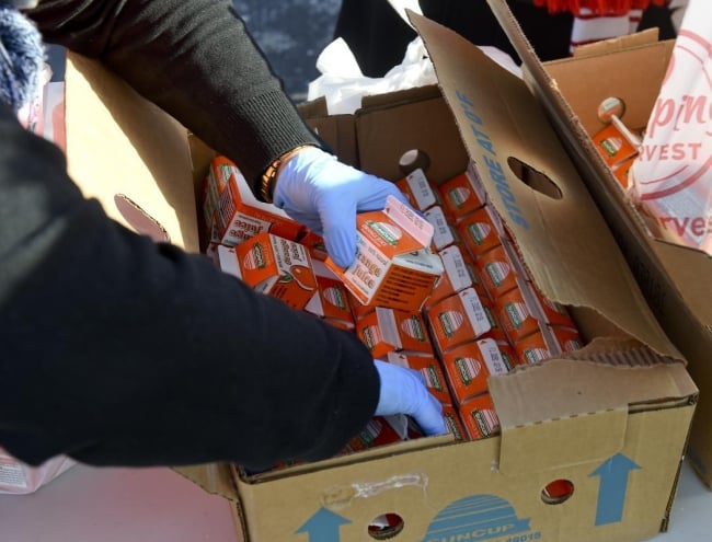 A photo of gloved hands sorting through a box of orange juice cartons.