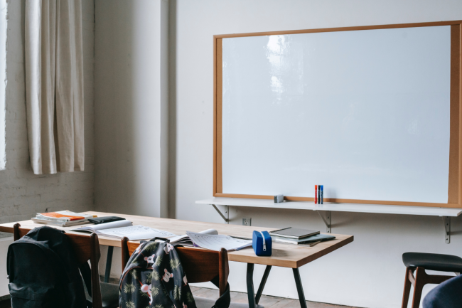 An empty classroom features a whiteboard and a desk with a black chair.