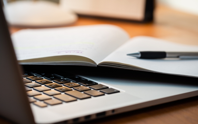 Laptop Computer on a Modern Wooden Business Desk with a Notepad and Pen in Unfocused Background