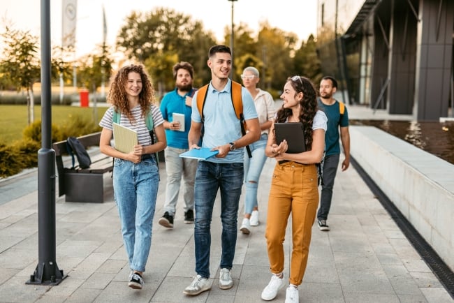 Group of friends walking on university campus, holding books and notebooks.