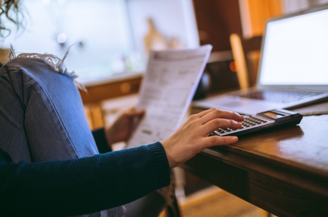 Close-up of a young woman using calculator, laptop and analyzing documents