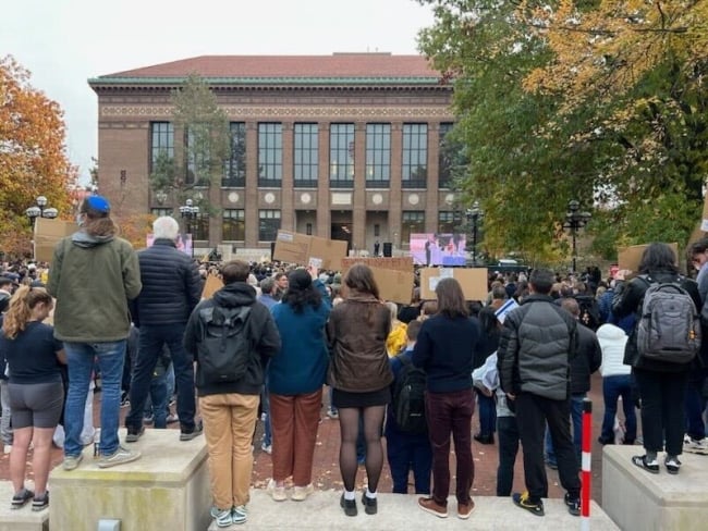 The backs of students holding signs outside of a large building.