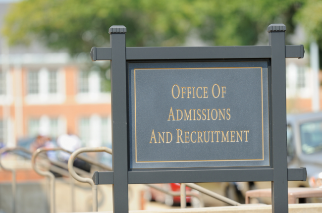 A black sign on a university campus that reads "Office of Admissions and Recruitment."