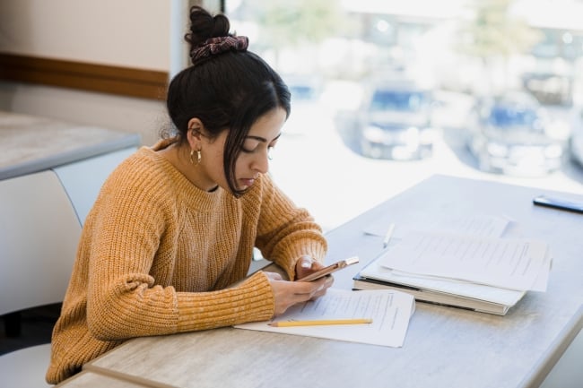 A student texts while working on homework at a desk