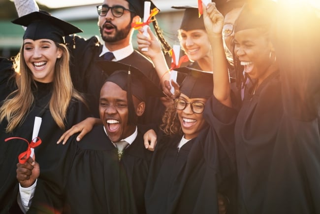 A group of students in graduation caps and gowns cheers. 