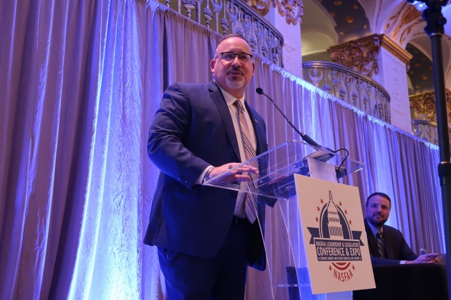 A Hispanic man in a suit at a podium