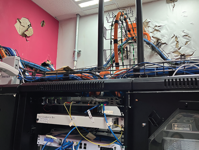 An image from the report of a college’s server room with wires everywhere and paint damage from Hurricane Maria. 