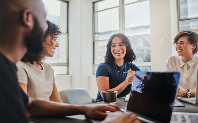 Group of young people smiling as they work together at a desk.