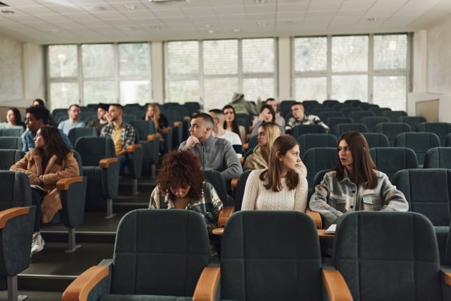 A large group of university students waiting for a class in an amphitheater.