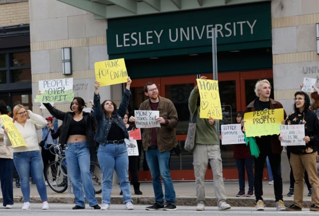 A photo of protestors holding signs objecting to job cuts at Lesley University.