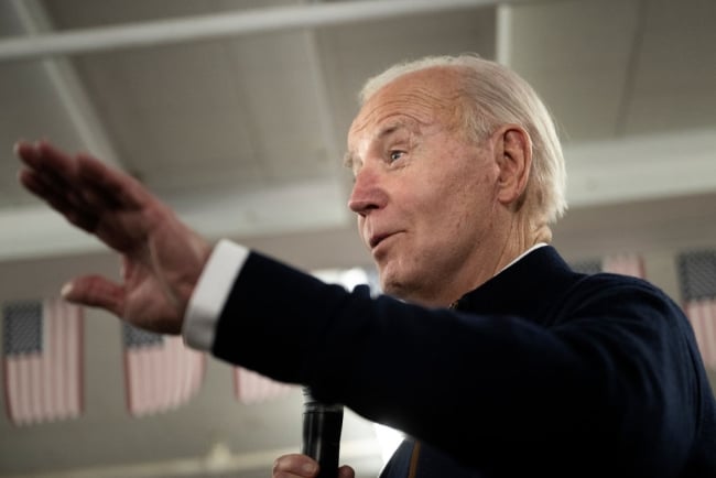 Biden extends a hand while speaking into a mic.