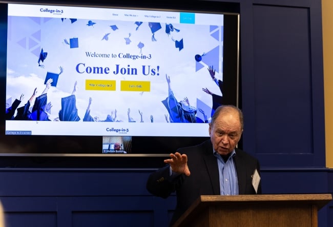 Man at dais in front of video screen