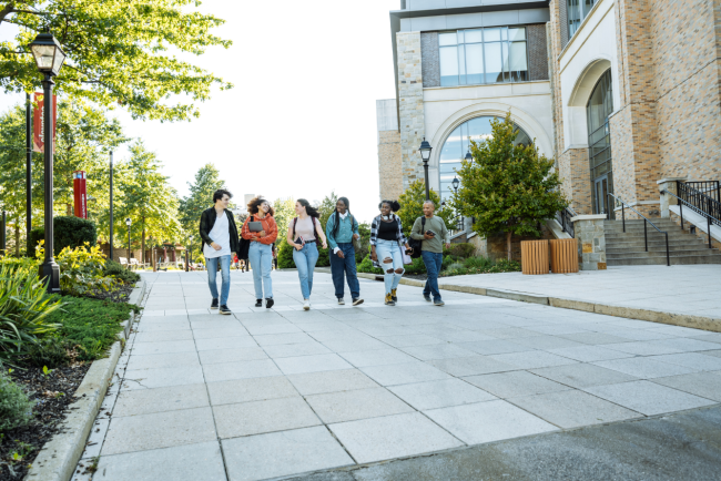 Six college students carrying backpacks and books walk on a campus.