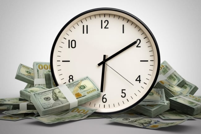 An analog clock sits nestled in between bound stacks of hundred dollar bills