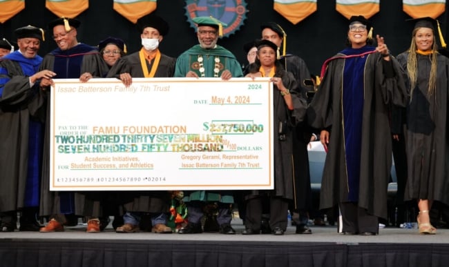 Professors in their ceremonial graduation garb holding a big check on a stage