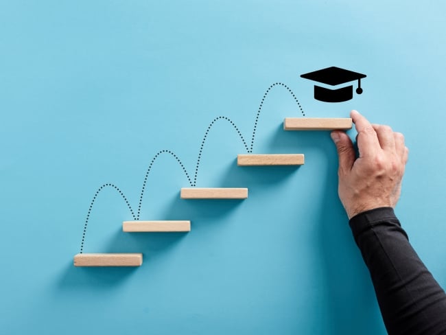 Male hand arranges a wooden block ladder with academic mortar board symbol at the top of the last step