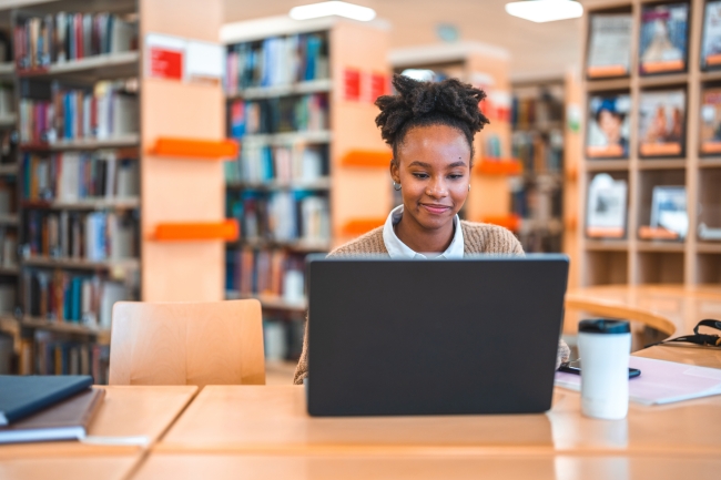 Young adult Hispanic female sitting at a desk in a library working on a computer