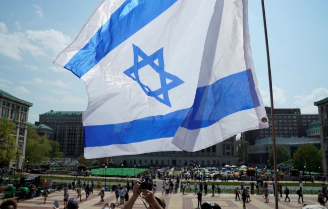 An Israeli flag waves in the foreground in a photo of Columbia University’s campus.