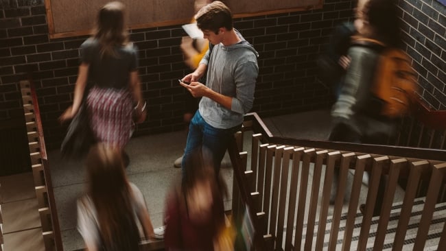 Young man focusing on his phone while other students pass by