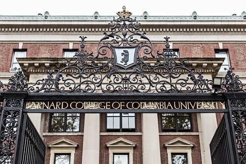The front gate of Barnard College. A brick building is in the background with a wrought iron fence in the front, which says "Barnard College of Columbia University" 