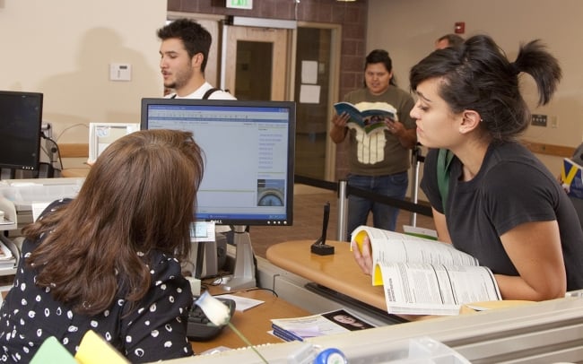 A student leans over a desk to look at a computer screen alongside a faculty member 